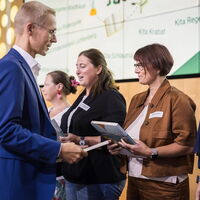 © André Wirsig; Dr. Tobias Ernst, Vorstand der Stiftung Kinder forschen, überreicht Wimmelbücher an Pädagoginnen zertifizierter Kindergärten und Horte, hier an Marion Czorny